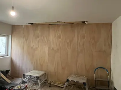 The same wall after the chimney breast was removed, now flat and lined with plywood sheets