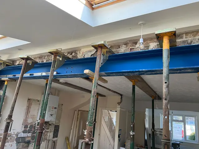 New blue steel beam held up on acrow props across the back of a house, with roof lights in the new ceiling above