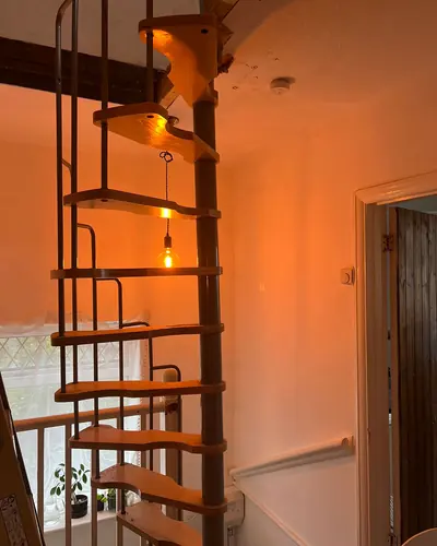 Spiral staircase with a steel column and timber treads rising through a landing ceiling into a loft