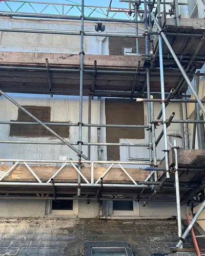 Scaffolding up the back of a tall rear wing, with patches of new render above a slate roof
